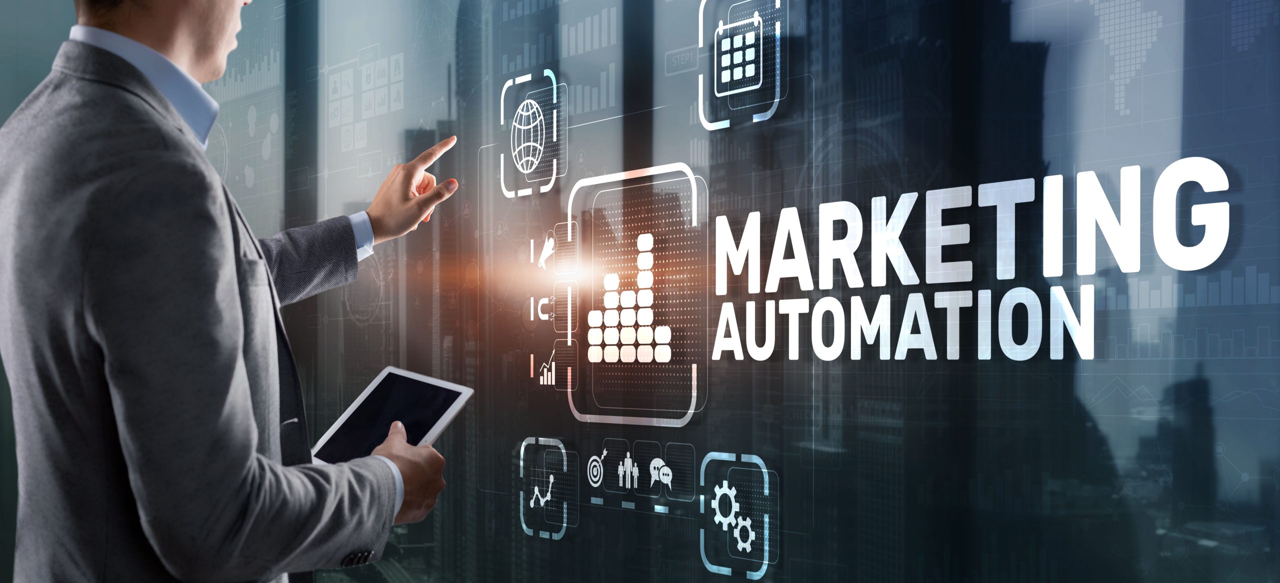Businessman touching a virtual screen with the text "MARKETING AUTOMATION" and related business technology icons, set against a blurred city backdrop.