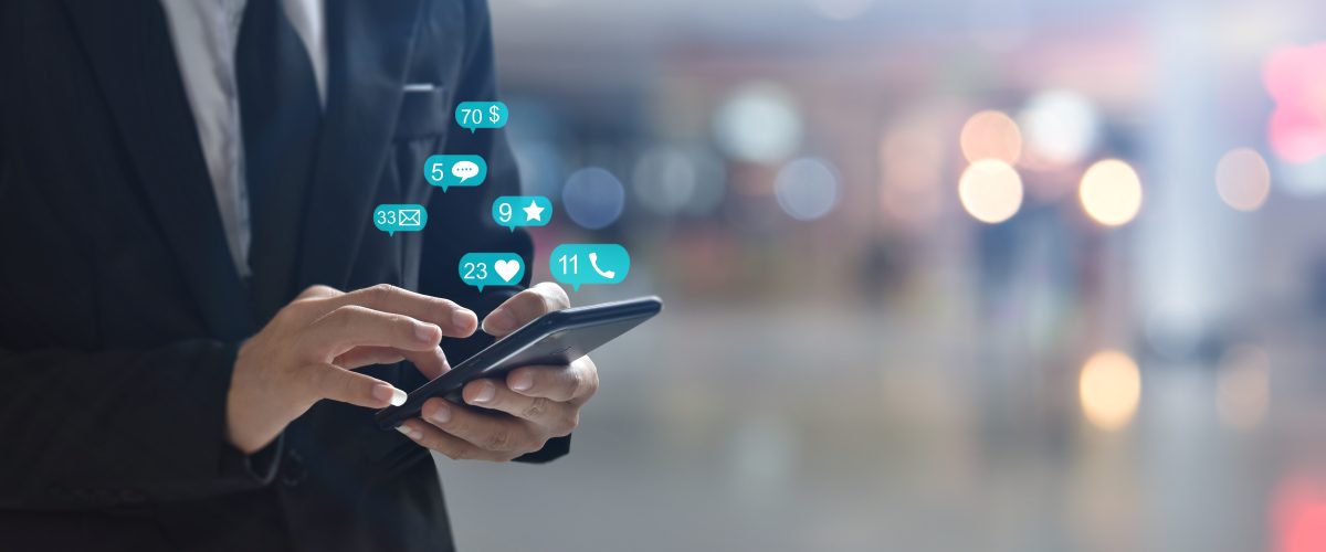 Close-up of a person's hands holding and tapping a smartphone, with colorful, glowing chat and social media icons floating above the screen, symbolizing digital communication and a conversational commerce platform.