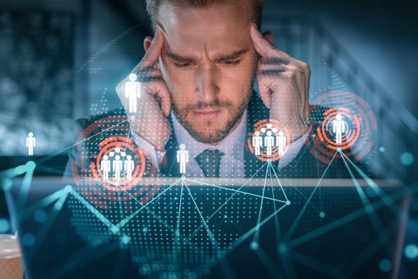 Handsome businessman in suit at workplace working with laptop to hire new employees for international business consulting. HR, social media hologram icons over office background